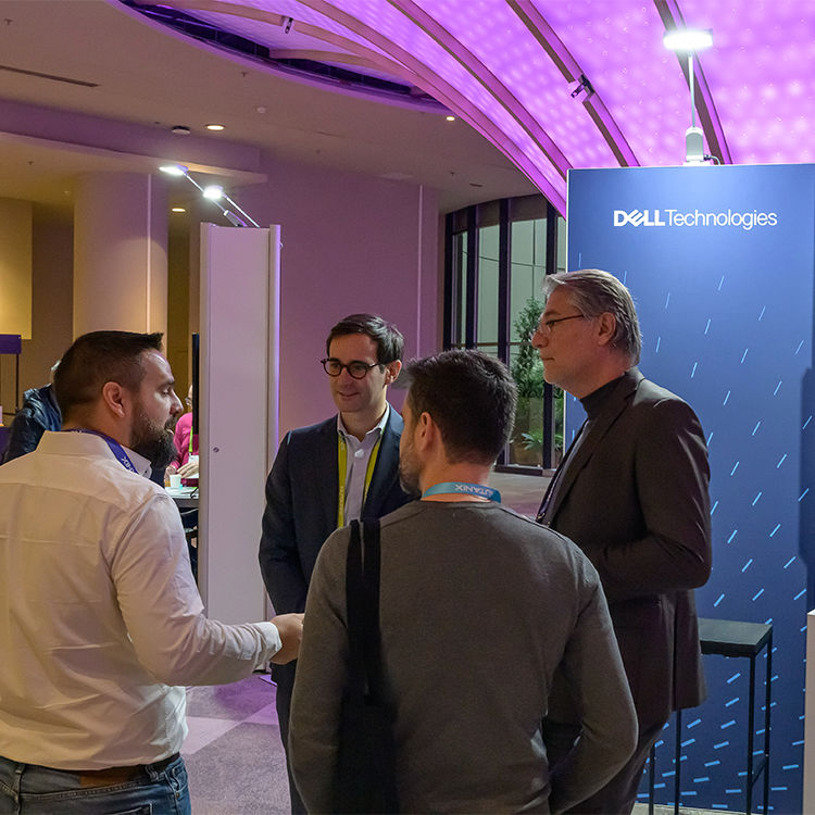 Group of four people engaged in conversation, standing together in front of a Dell Technologies banner.